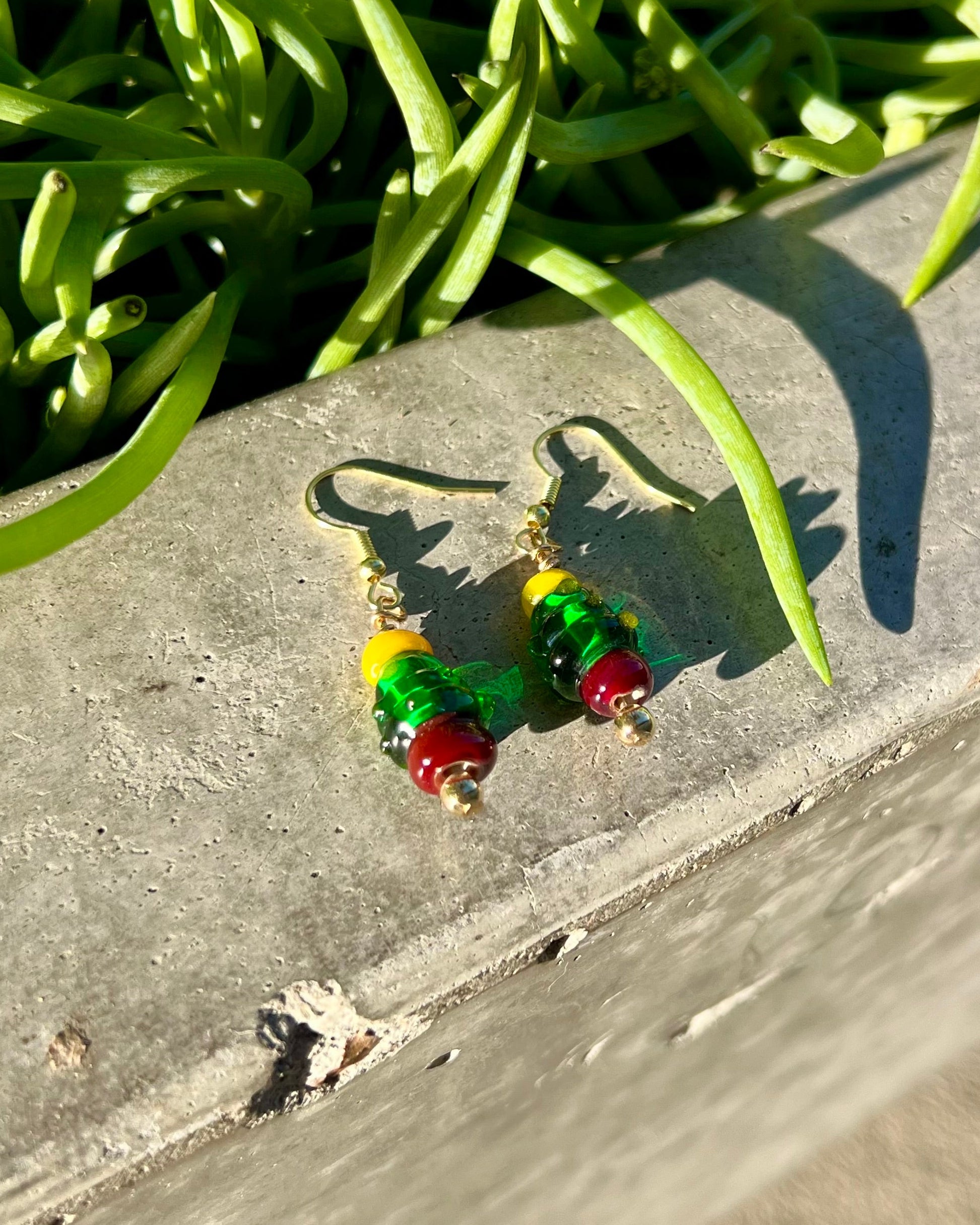 christmas tree earrings on a concrete surface with green plants in the background