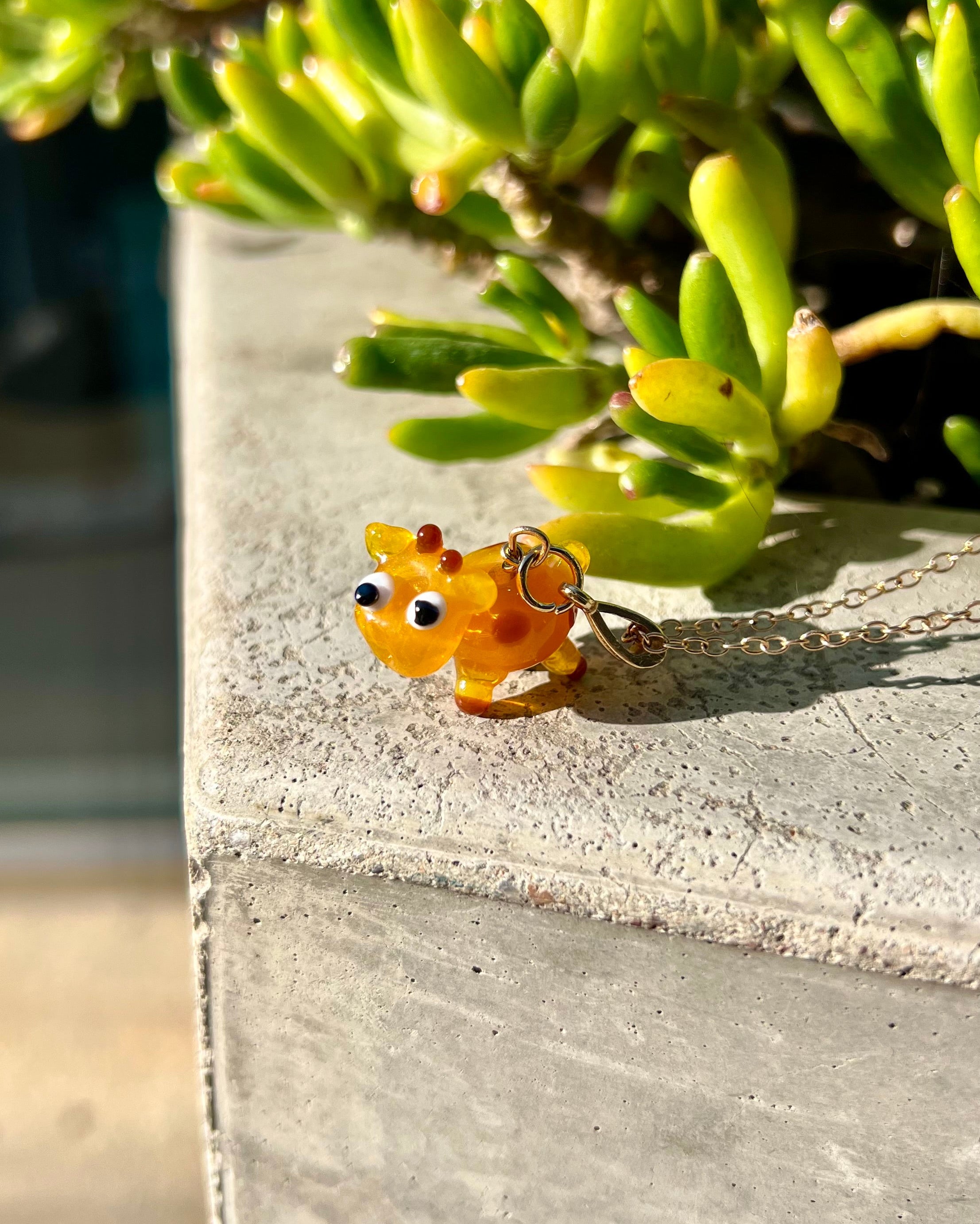 Small yellow creature figurine on a chain against a green plant background