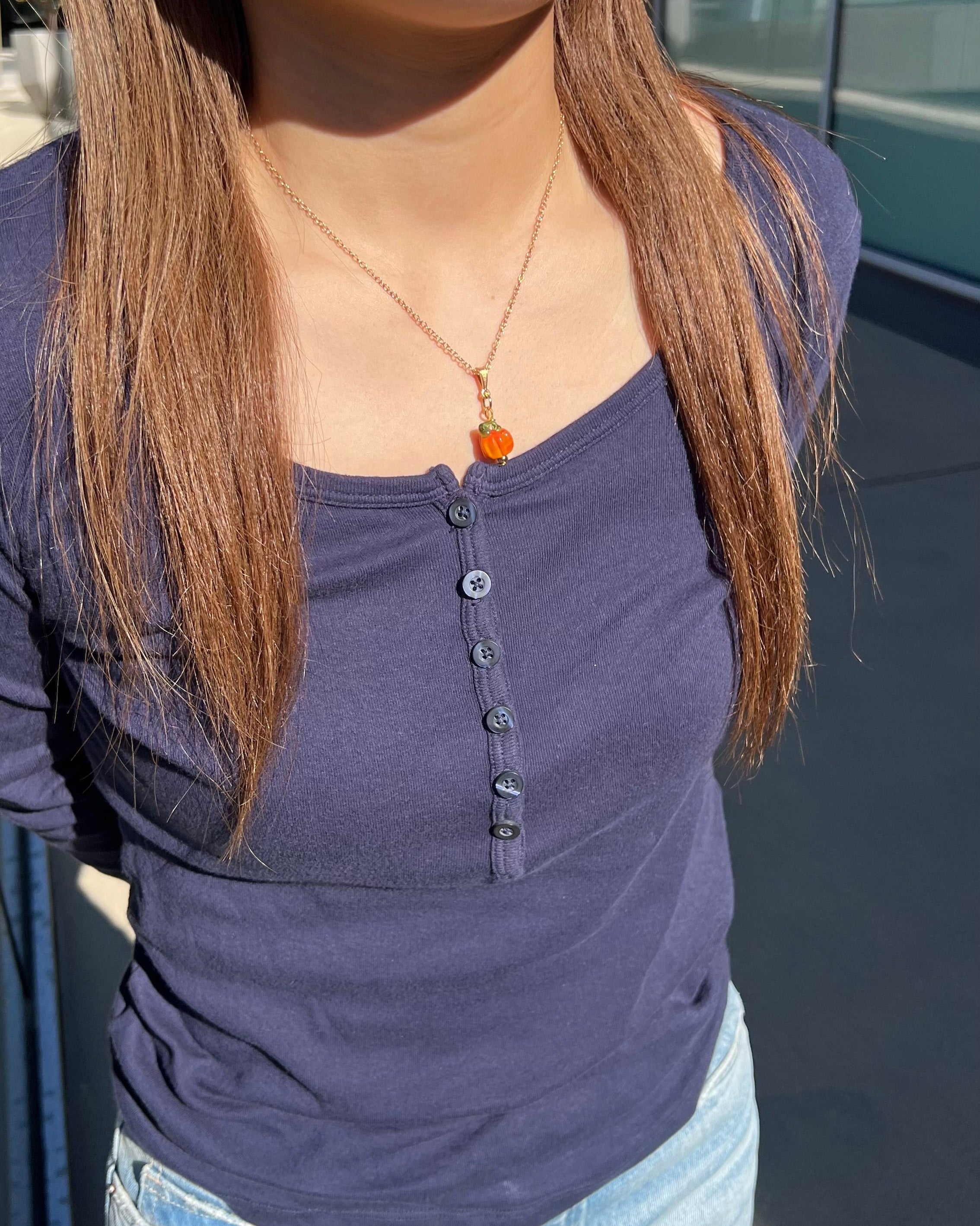 Person wearing a purple shirt and blue jeans with a necklace featuring an orange pendant.