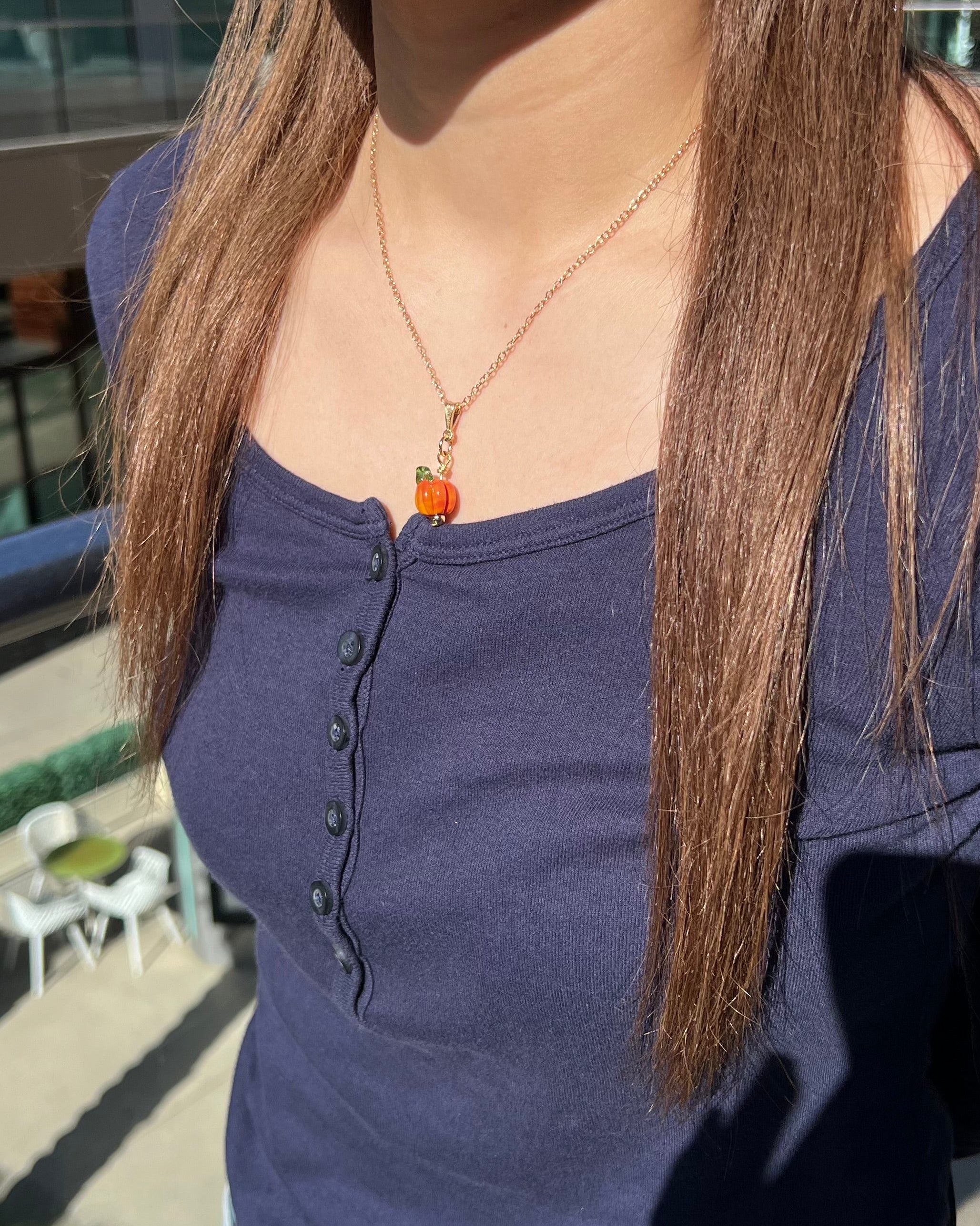 Person wearing a blue shirt with a necklace featuring an orange charm, standing outdoors.