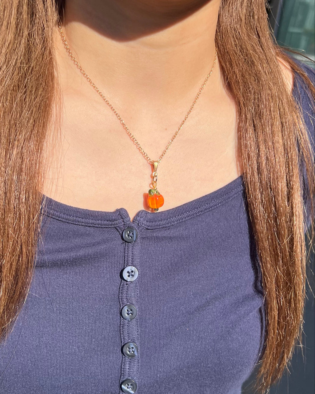 Person wearing a necklace with an orange pendant, standing outdoors.