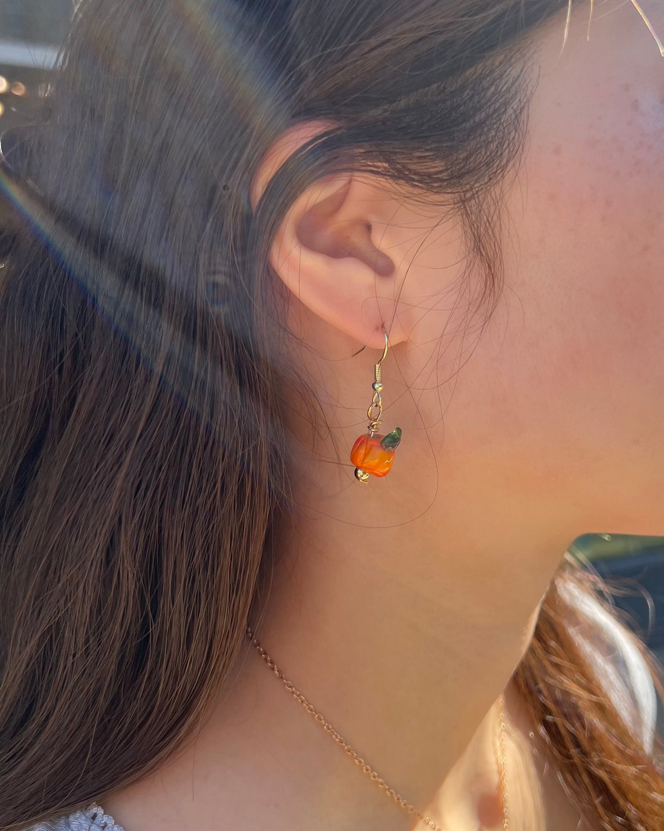 Close-up of a person wearing a small earring with a colorful bead.