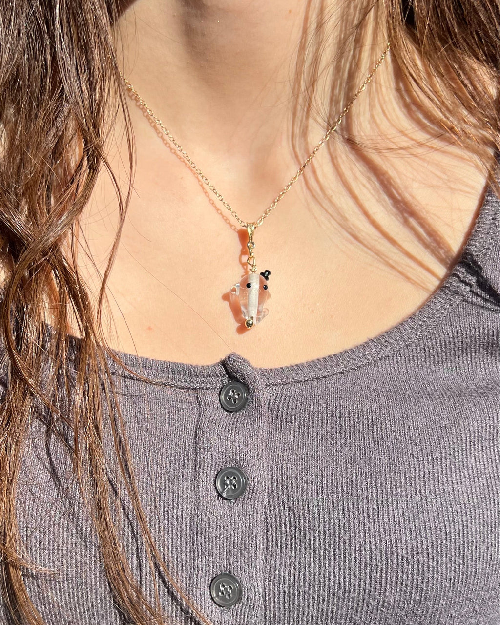 Person wearing a necklace with a pendant, close-up of neck and chest area.