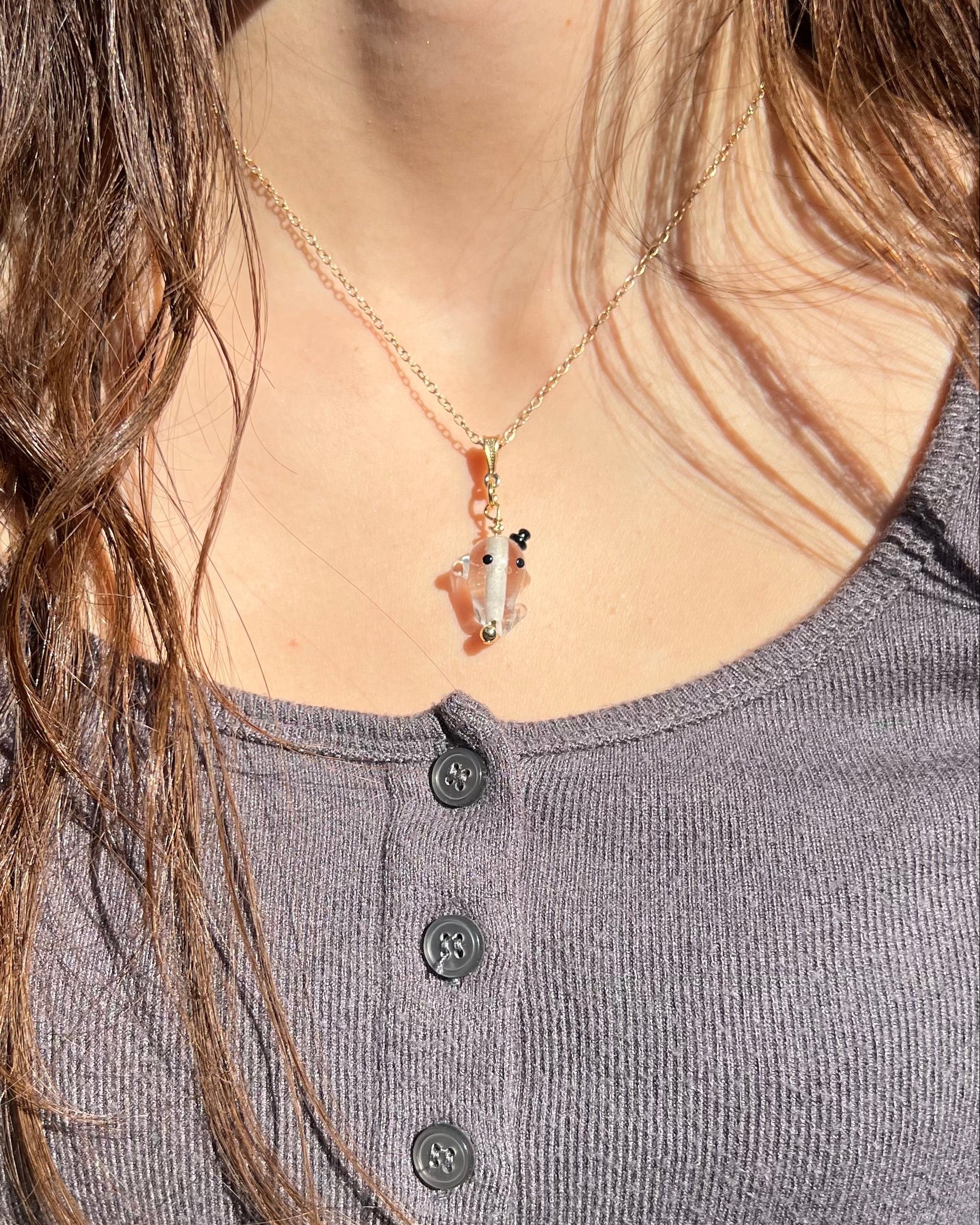 Person wearing a necklace with a pendant, close-up of neck and chest area.